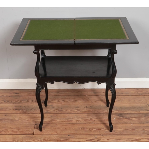 573 - An Art Nouveau style ebonized fold-over games table with lower tier. Approx. dimensions when folded ... 