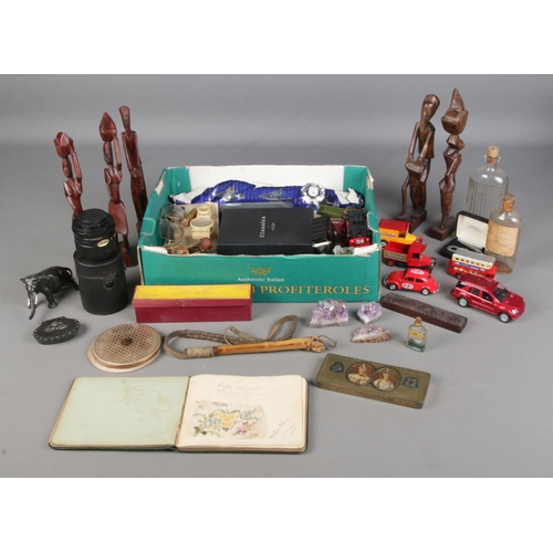 406 - A box of collectables. Includes wooden tribal figures, pens, diecast vehicles, chemist bottles, souv... 