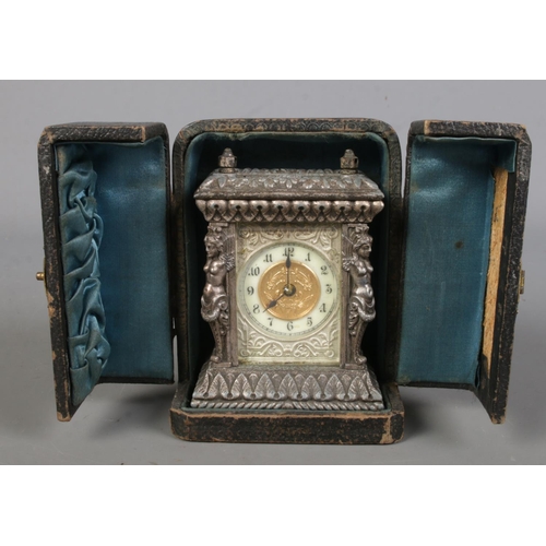 540 - An ornate metal miniature desk clock in fitted leather case. (9cm)