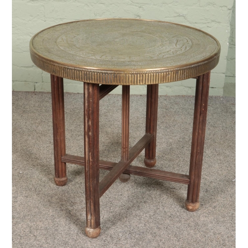 583 - An Indian brass top table with folding wooden base. Diameter of top 60cm.