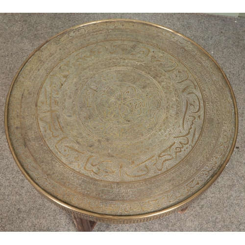 583 - An Indian brass top table with folding wooden base. Diameter of top 60cm.