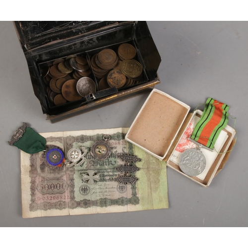 437 - A tin cash box with contents of coins and medals. Includes The Defence Medal, silver cycling medal a... 