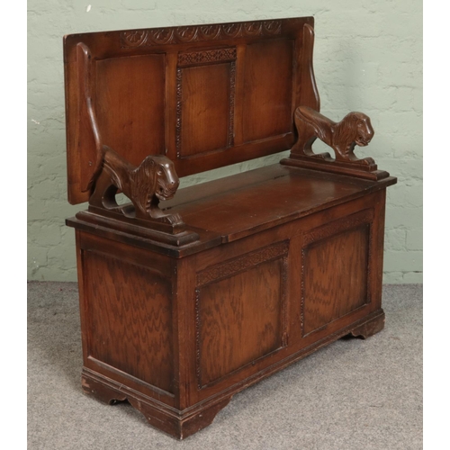 566 - A carved and panelled oak monks bench. With lion mask handles and under seat storage.