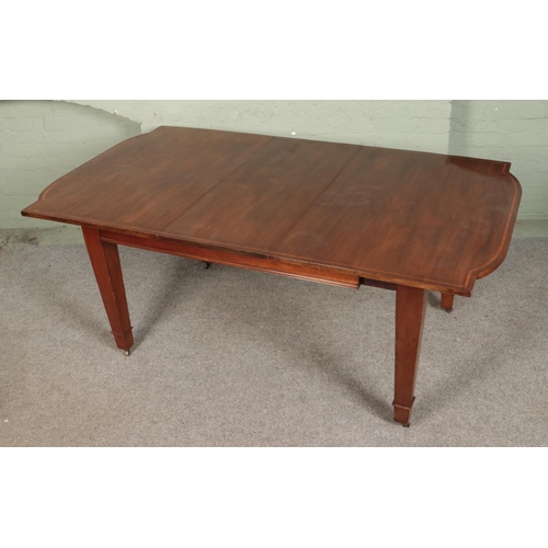 589 - A mahogany inlaid dining table with square tapering legs sat on brass castors. Comes with one additi... 