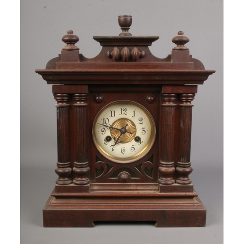 52 - An oak cased mantel clock with brass and enamel dial flanked by twin pillars. Includes key and pendu... 