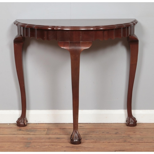 480 - A mahogany demi-lune console table, with waved edging and three ball and claw feet. Bearing label fo... 