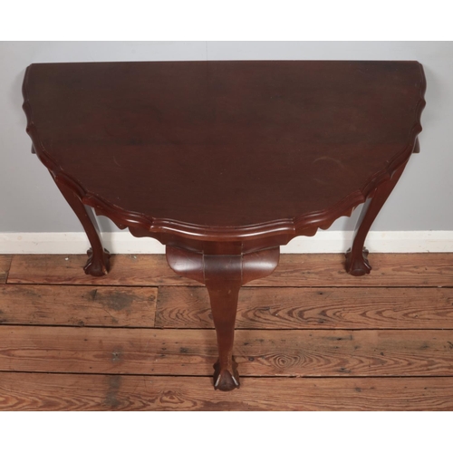 480 - A mahogany demi-lune console table, with waved edging and three ball and claw feet. Bearing label fo... 