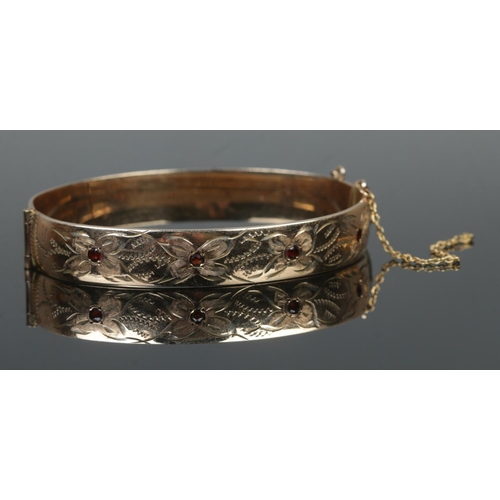 393 - A 9ct rolled gold hinged bangle, set with four garnet stones and half engraved detailing.