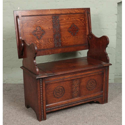 517 - A carved oak monks bench, with detailing to back rest and front. Featuring folding top and under sea... 