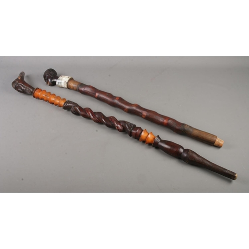 107 - Two tribal style walking sticks both with carved detail depicting tribesmen one with cow horn detail... 