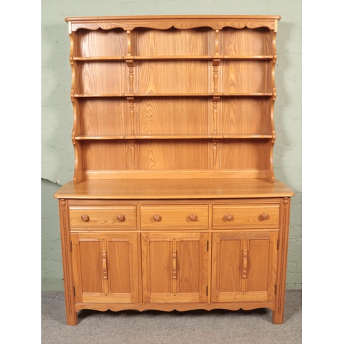 560 - An Ercol light oak Welsh dresser, with cupboard doors and drawers to the base and plate rack top. He... 