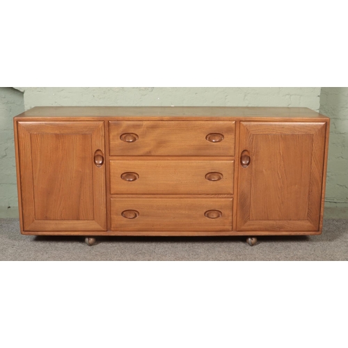 562 - An Ercol light elm Windsor sideboard with three drawers flanked by cupboard doors. The top drawer be... 