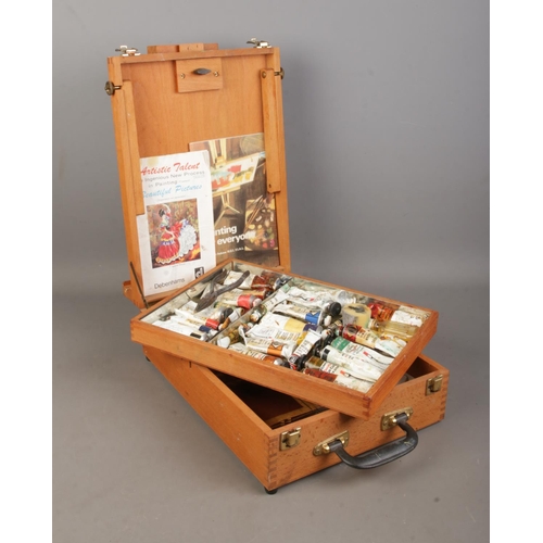 69 - A wooden artist's box, with hinged top and folding easel back. Containing a collection of paints, in... 