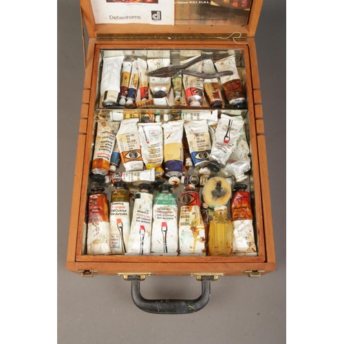 69 - A wooden artist's box, with hinged top and folding easel back. Containing a collection of paints, in... 