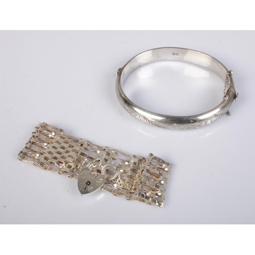 438 - A silver tulip engraved bangle along with silver gate bracelet with heart lock. Total weight 31.5g.