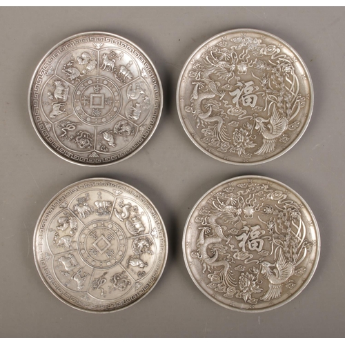 473 - A set of four decorative Oriental white metal coasters featuring dragon and Phoenix motifs along wit... 