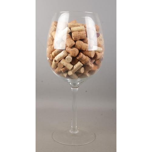 65 - A large wine glass with contents of corks. Height of glass 49.5cm.