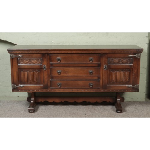 557 - An old charm oak carved sideboard with linen fold detail on doors flanking three drawers.