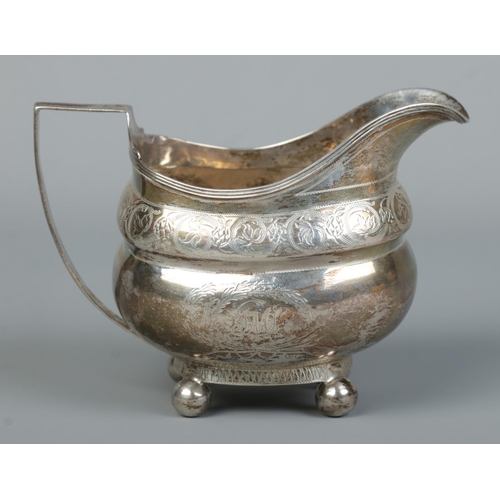 127 - A Georgian silver cream jug with engraved decoration and raised on four ball feet. Bearing London ma... 