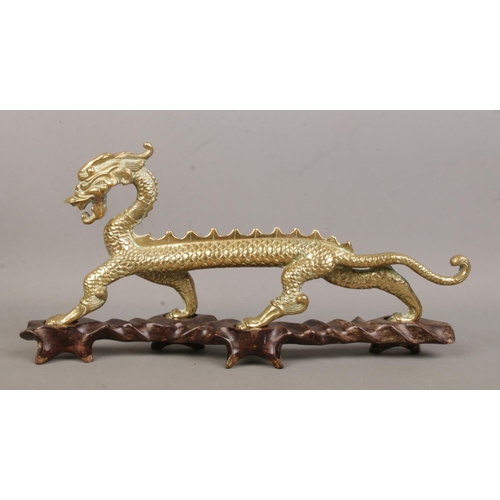 8 - A brass figure of a Chinese dragon raised on hardwood stand. Height 16cm, Length 34cm.