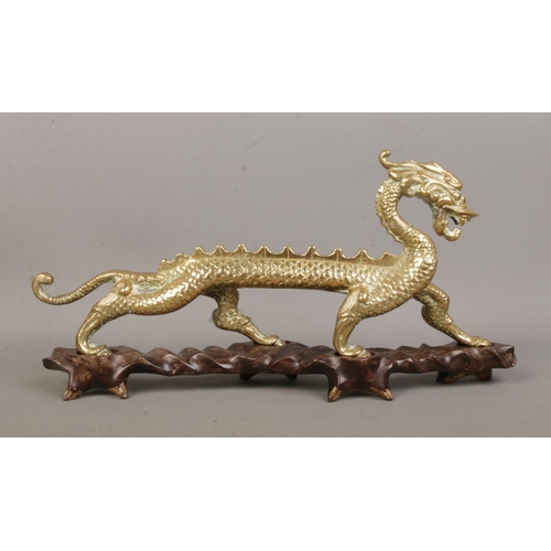 8 - A brass figure of a Chinese dragon raised on hardwood stand. Height 16cm, Length 34cm.