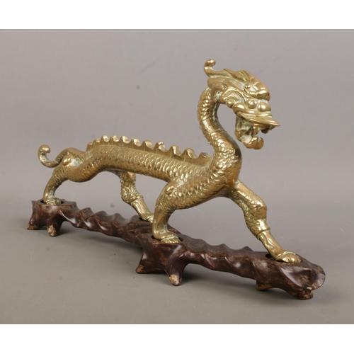 8 - A brass figure of a Chinese dragon raised on hardwood stand. Height 16cm, Length 34cm.