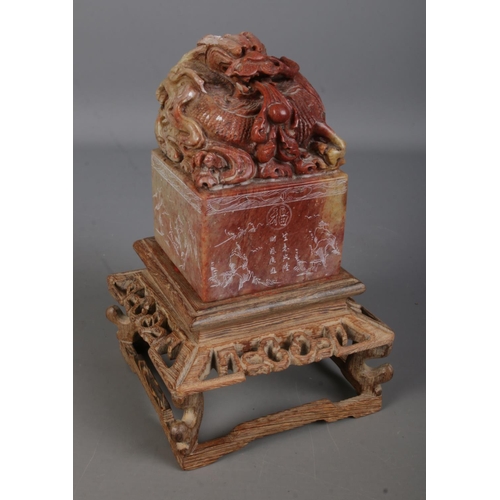 555 - A Chinese carved soapstone seal on carved wooden stand. The seal surmounted with a Qilin with sides ... 