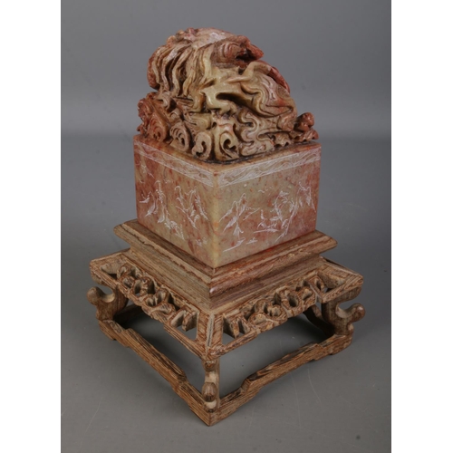 555 - A Chinese carved soapstone seal on carved wooden stand. The seal surmounted with a Qilin with sides ... 