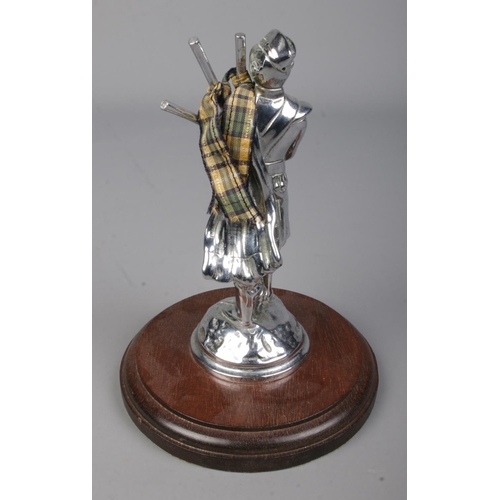 566 - A chrome car mascot formed as a Scottish Bagpiper, mounted on wooden base. Approx. height 16cm.