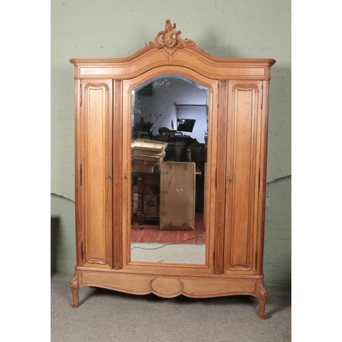 606 - A large oak three door armoire with ornate carved acanthus and c-scroll crest above a mirrored arche... 