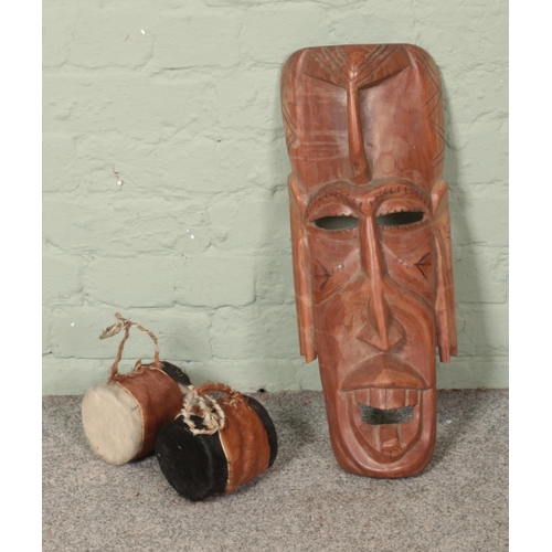 110 - A collection of tribal to include large wall hanging carved mask and two miniature cow hide drums.