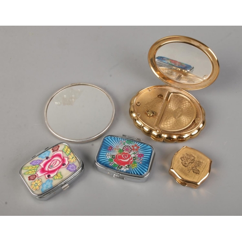 142 - A silver circular hand mirror along with a Minuette musical compact and three pill boxes. The mirror... 