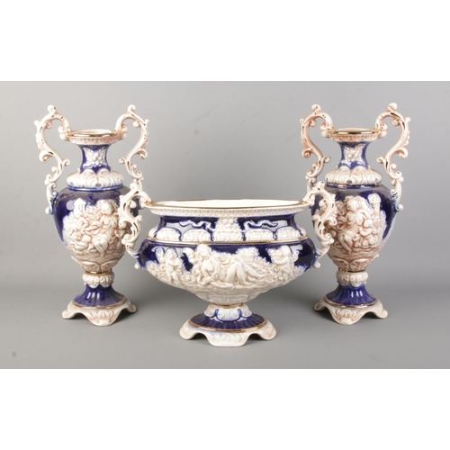 162 - An Italian pottery garniture. Relief moulded with putti and maidens. Height of tallest pieces 38cm.