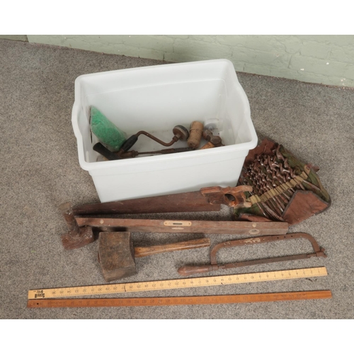 241 - A box of assorted tools. Includes two wooden metre rulers, wooden mallet, hand saw, drill bits etc.