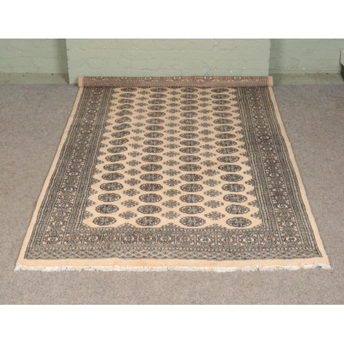 302 - A fawn coloured wool rug, with fringed edge, featuring stylised geometrical decoration. Length: 252c... 