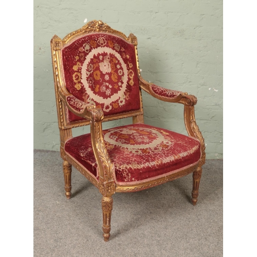 529 - A carved and gilt painted throne armchair, with floral red upholstery and arm pads.