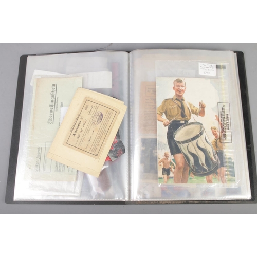 455 - A folder holding a collection of war time militaria including Hitler Youth documents, cuff titles, f... 