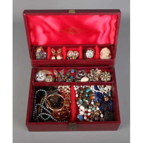 56 - A deep red cantilever jewellery box containing costume jewellery. Includes belt buckle, brooches, la... 