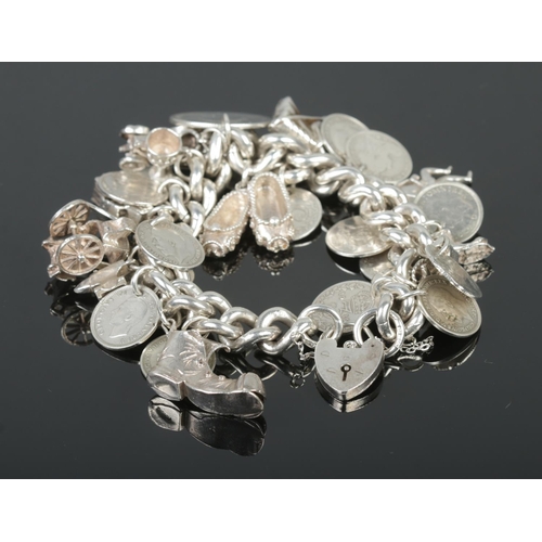 427 - A heavy silver charm bracelet with heart-shaped clasp, containing an assortment of silver and white ... 