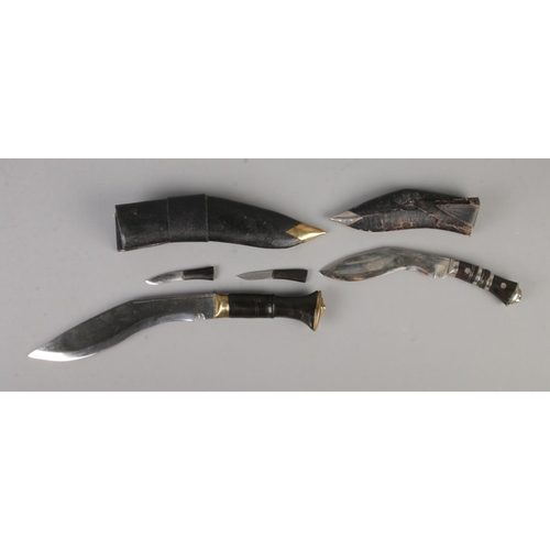 98 - Two Indian Kukri knives on display stand with larger knife featuring two small accompanying knives. ... 