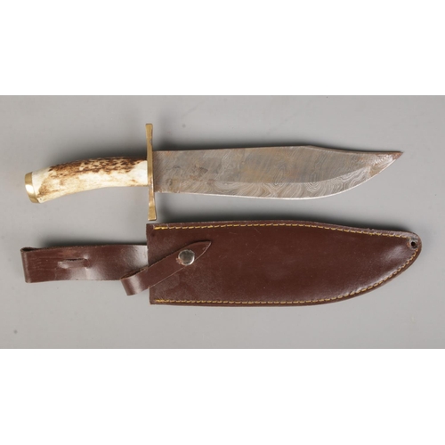 399 - A horn handled bowie knife with sheath featuring Damascus blade and brass cross guard. CANNOT POST.