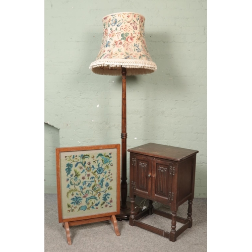 454 - A small carved linen fold cabinet along with a turned mahogany standard lamp and an embroided firesc... 