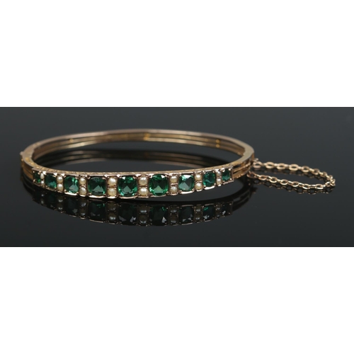 152 - A Victorian 9ct gold bangle set with green coloured stones and seed pearls. 8.6g.