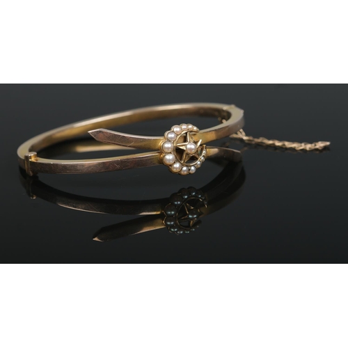 155 - A 9ct gold bangle with crescent and star decoration set with seed pearls. 8.76g.