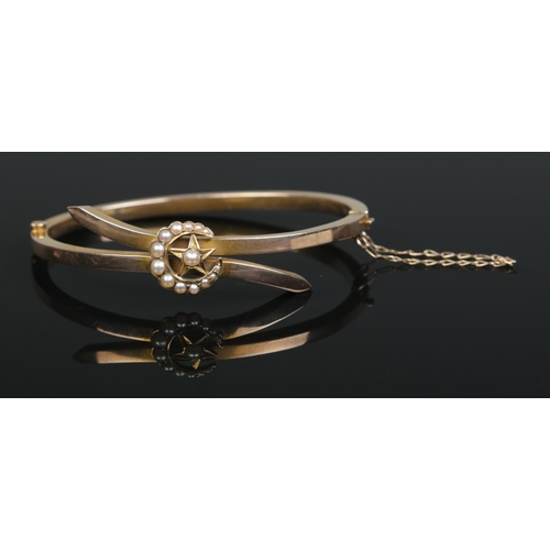 155 - A 9ct gold bangle with crescent and star decoration set with seed pearls. 8.76g.