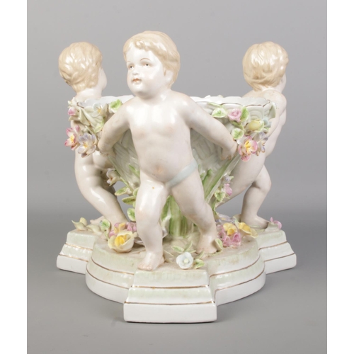 49 - A continental porcelain centrepiece formed as three cherubs holding a bowl. Height 24.5cm.