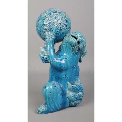 64 - A Japanese turquoise glaze lion dog in seated position holding a ball in its front paws. Height 25cm... 