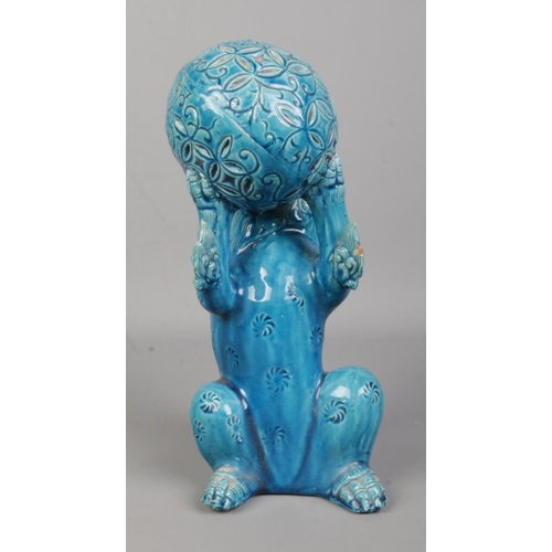 64 - A Japanese turquoise glaze lion dog in seated position holding a ball in its front paws. Height 25cm... 