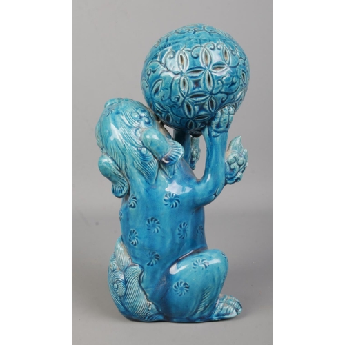 64 - A Japanese turquoise glaze lion dog in seated position holding a ball in its front paws. Height 25cm... 