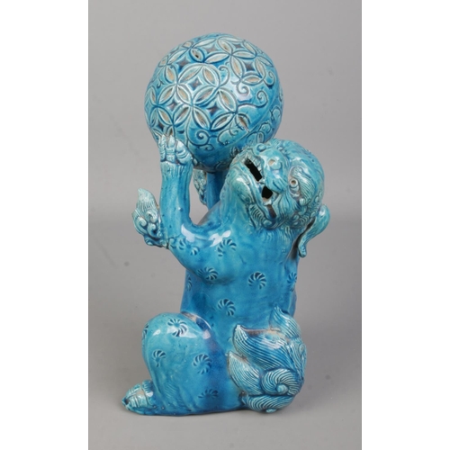 64 - A Japanese turquoise glaze lion dog in seated position holding a ball in its front paws. Height 25cm... 